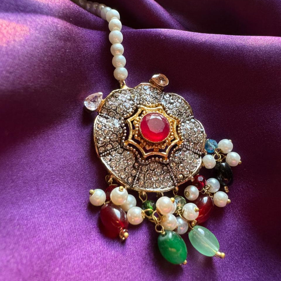 Intricate traditional pendant with red gem, pearls, and multicolored beads on purple fabric